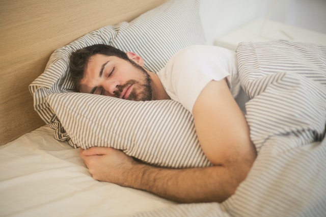 Muž spí zakrytý paplónom v posteli